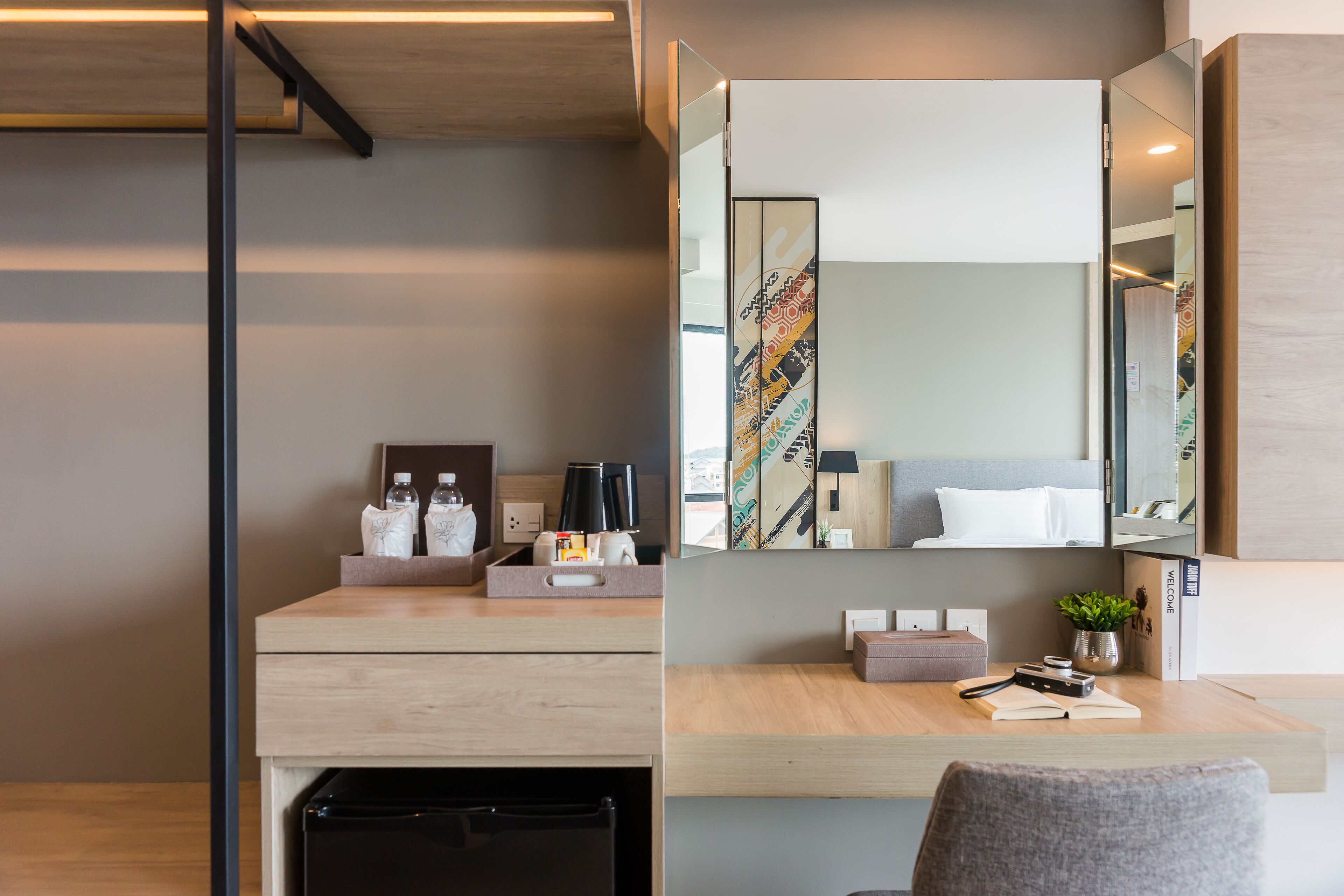 A modern hotel room with a wooden desk, a black trash bin, a mirror, and a small potted plant.