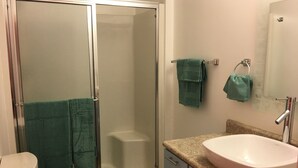 A bathroom with a toilet, a shower with a glass door, a sink, and two towels hanging on hooks. - Aquamarine Upbeat Studio on the Mall  (Kodiak)