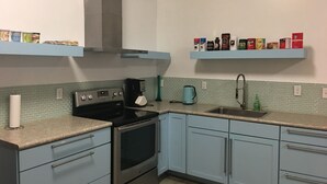 A kitchen with light blue cabinets, a stainless steel stove, a coffee maker, and shelves with various coffee and tea products. - Aquamarine Upbeat Studio on the Mall  (Kodiak)
