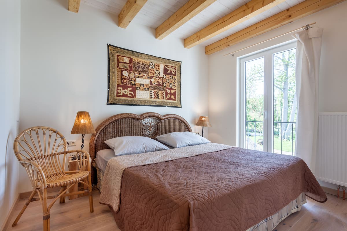 Quarto com uma cama grande, uma cadeira de vime, tapeçaria na parede e uma janela com cortinas.