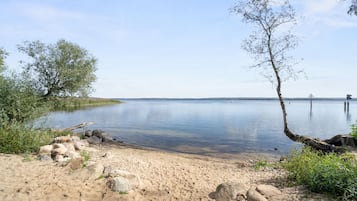 A calm lake with clear water, surrounded by sandy shores and sparse vegetation.