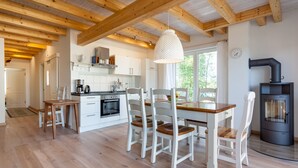 A modern kitchen with wooden beams, white cabinetry, a dining table with chairs, and a wood-burning stove. - Plau Lagoons (Plau am See)