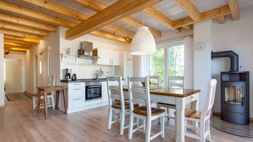 A modern kitchen with wooden beams, white cabinetry, a dining table with chairs, and a wood-burning stove.