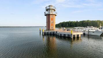A lighthouse on a dock with boats and a forested shoreline.