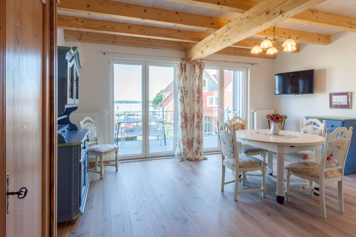 Uma sala de jantar com teto de madeira, uma mesa com cadeiras estampadas e vista através das portas de vidro.