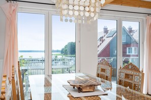 Ein Zimmer mit großem Fenster, einem Holzkopfteil, einem Tisch mit Schachbrett und einer Pendelleuchte.