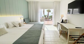 Habitació d'hotel amb dos llits, un escriptori, una televisió i vista a palmeres.