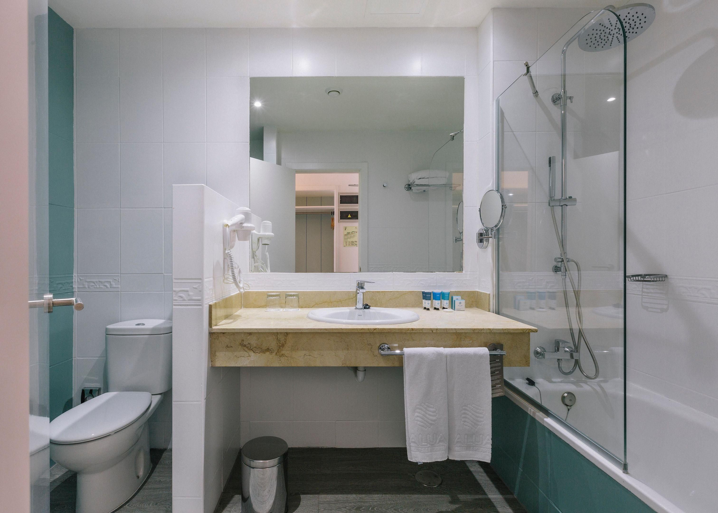 A bathroom with a toilet, sink, mirror, and shower.