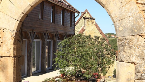 An arched stone structure framing a building with a tiled roof and a garden with flowers. - Cottage for 2 or 4 p refurbished in an old fortified farm from the 17th century (Saint-Amand-de-Coly)