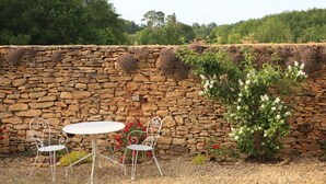 A stone wall with climbing plants, a white metal table, and two chairs in a garden setting. - Cottage for 2 or 4 p refurbished in an old fortified farm from the 17th century (Saint-Amand-de-Coly)