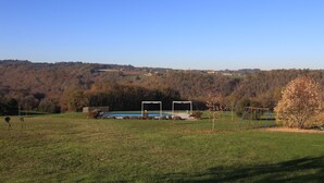 A grassy field with a playground, a small building, and a forested hill in the background. - Cottage for 2 or 4 p refurbished in an old fortified farm from the 17th century (Saint-Amand-de-Coly)