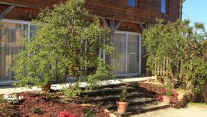 A wooden building with a large window and a garden with various plants and flowers. - Cottage for 2 or 4 p refurbished in an old fortified farm from the 17th century (Saint-Amand-de-Coly)