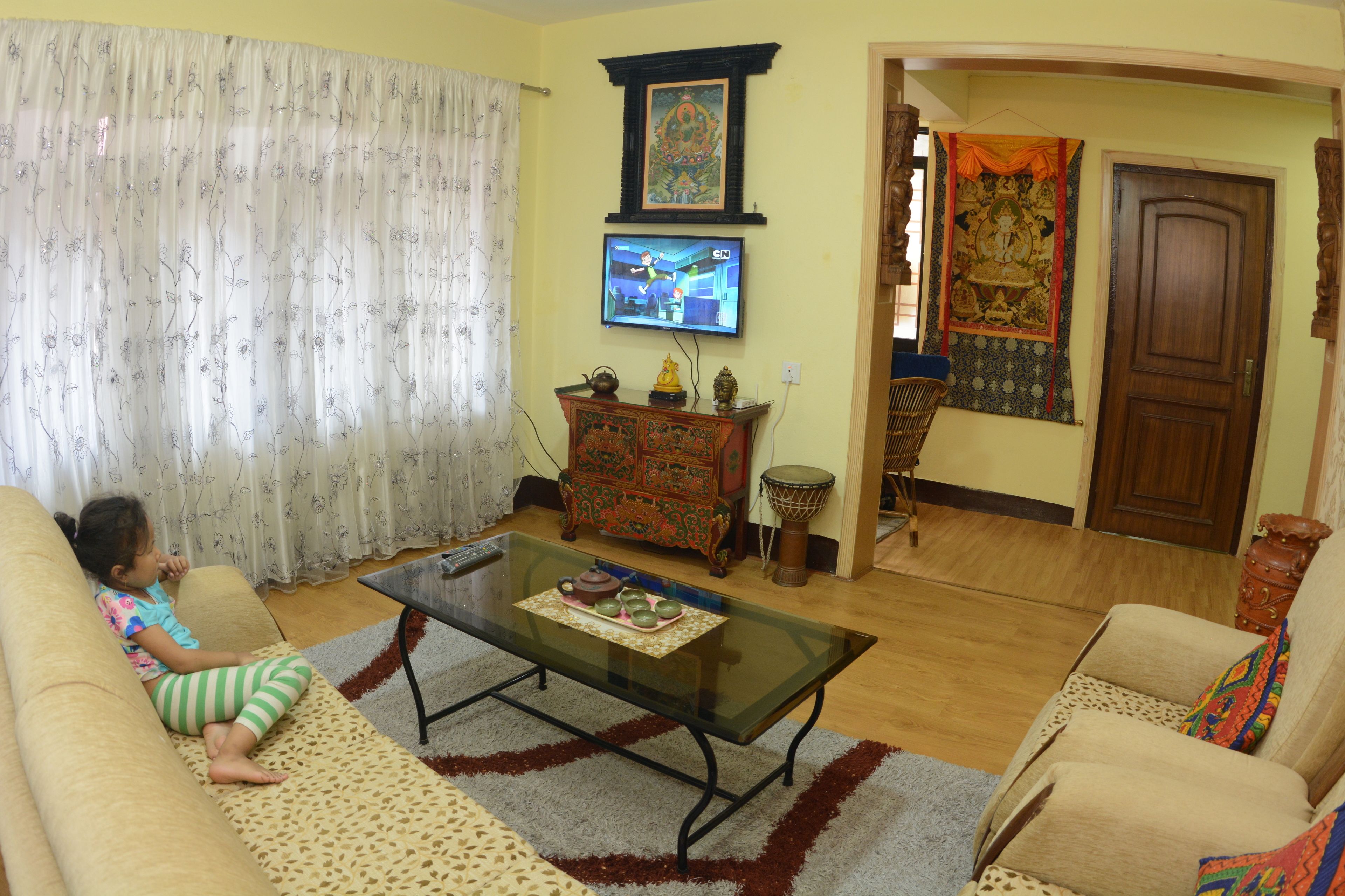 A living room with a sofa, a glass coffee table, a television, a decorative cabinet, and a door.