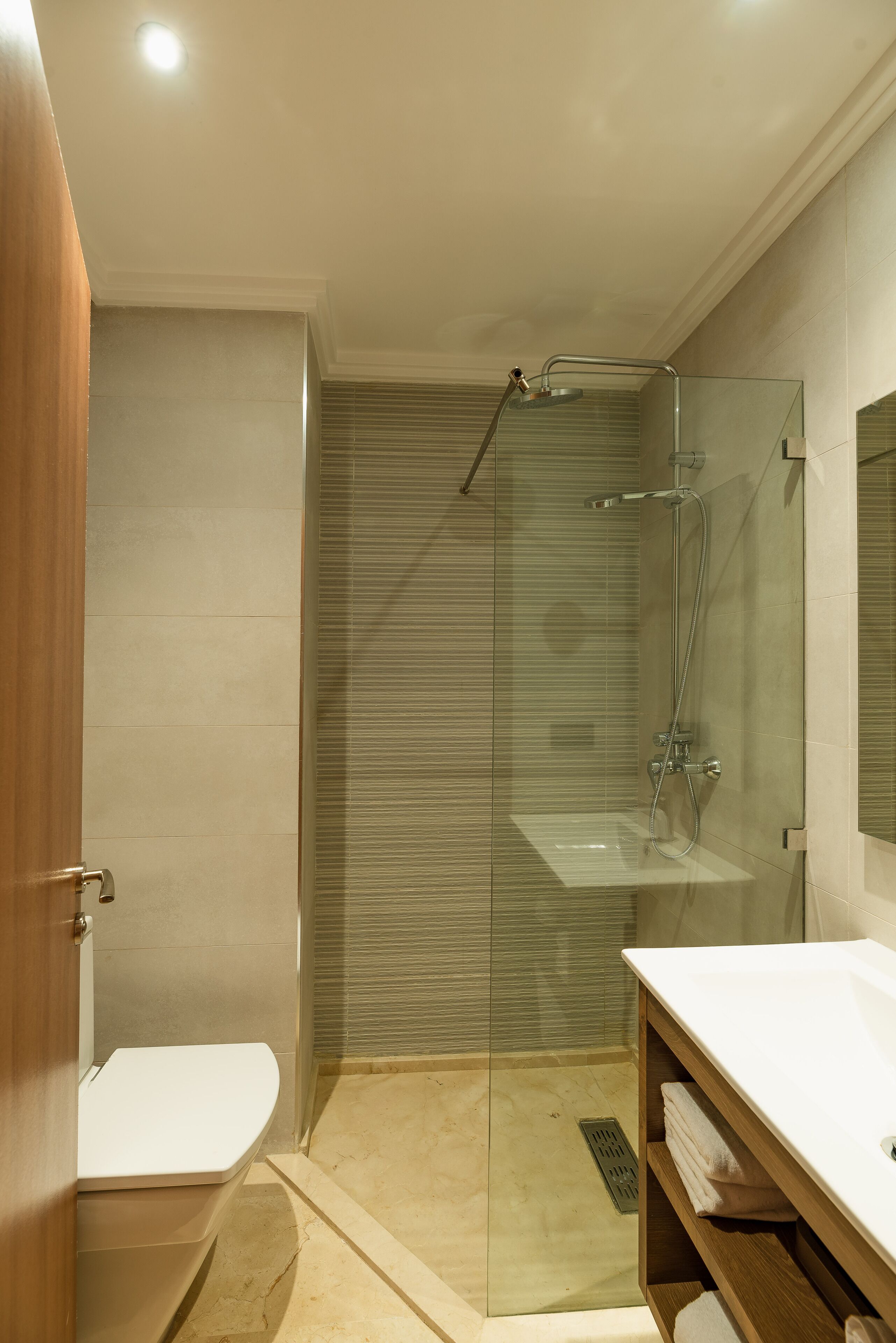 A modern bathroom with a glass shower enclosure, a white sink, and a wooden vanity.