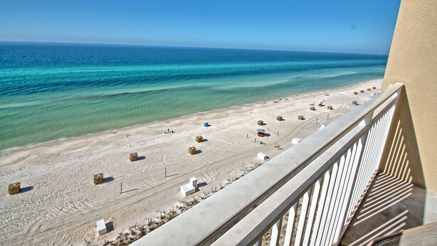 A beach view from a balcony with clear skies, a sandy beach, and some beach furniture.