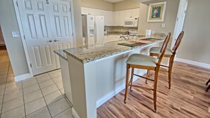 A kitchen with white cabinets, a granite countertop, and wooden chairs.