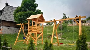 A wooden swing set with a ladder and a small wooden structure, surrounded by a wooden fence and greenery. - Lodge Nagramak (Bajina Bašta)