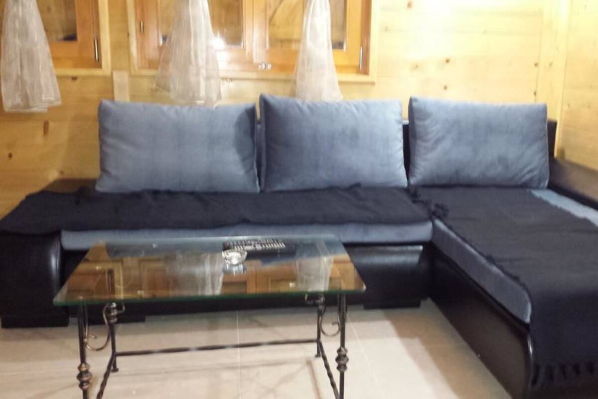 A wooden interior with a black sofa and glass coffee table.