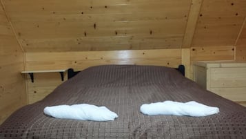 A wooden cabin-style room with a bed, two pillows, and a small wooden cabinet.