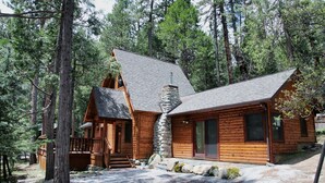 Una cabaña de troncos con chimenea de piedra, terraza de madera y pared de piedra.
