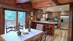 Un interior de madera con una mesa de comedor, sillas, un reloj y una zona de cocina que incluye un refrigerador y un microondas.