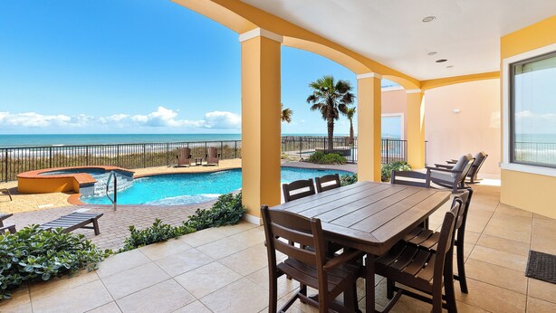 A pool area with a view of the ocean, a dining table with chairs, and a lounge area.