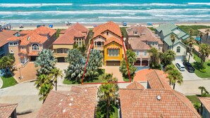 A coastal residential area with houses featuring red-tiled roofs, a central yellow house with a large garage, and a view of the ocean.
