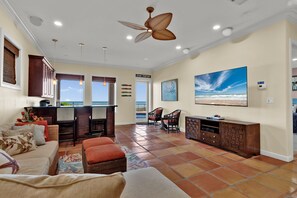 A spacious living area with a large window, a ceiling fan, and a television mounted on the wall.