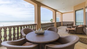 A balcony with a view of the beach, wicker furniture, and a glass door.