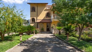A two-story building with a central entrance, surrounded by greenery and a gravel path. - 2 BEDROOM APARTMENT WITH A VIEW OF THE GULF OF NAPLES (Sant'Agnello)