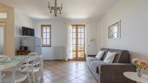 A spacious living area with a grey sofa, a dining table with chairs, a TV mounted on the wall, and a chandelier. - 2 BEDROOM APARTMENT WITH A VIEW OF THE GULF OF NAPLES (Sant'Agnello)