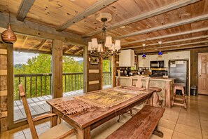 Cocina rústica con vigas de madera, una amplia mesa de madera y vistas al verdor exterior.