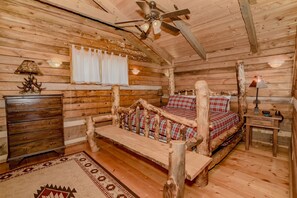 Un dormitorio de cabaña de troncos con una cama de madera, un ventilador de techo, un aparador y una alfombra.