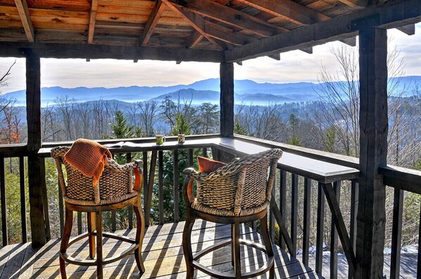 A wooden deck with two wicker chairs facing a scenic mountain view.