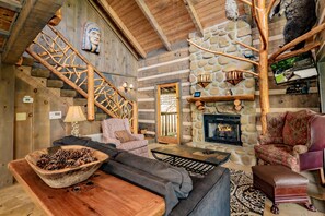 A rustic interior with a stone fireplace, wooden staircase, and cozy seating areas.