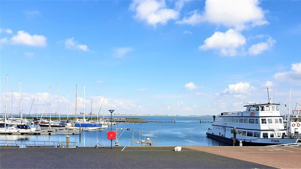 A marina with boats docked, a large white boat named 'frisia' in the foreground, and a clear blue sky. - Vacation apartment L' Ancora (mill view) (sint-annaland)