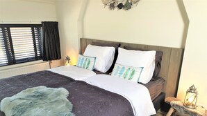A neatly made bed with a grey and white duvet, a fluffy throw, and decorative pillows. A small wooden nightstand with a lantern is beside the bed. - Vacation apartment L' Ancora (mill view) (sint-annaland)