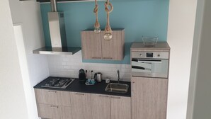 A modern kitchen with light wood cabinets, a black countertop, stainless steel appliances, and a blue accent wall. - Vacation apartment L' Ancora (mill view) (sint-annaland)