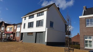 A two-story residential building with a white facade, grey garage doors, and a brick chimney. - Vacation apartment L' Ancora (mill view) (sint-annaland)
