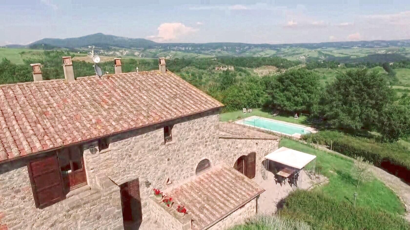 Un edificio de piedra con tejado de tejas, piscina y vistas a colinas verdes.