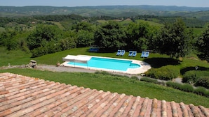 Ein Swimmingpool mit blauen Stühlen, umgeben von üppiger Vegetation und Hügeln im Hintergrund.