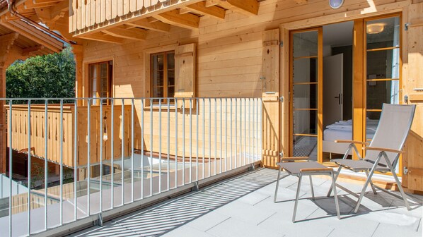 Una cabaña de madera con balcón, una puerta de vidrio que da al interior y una silla en la terraza.