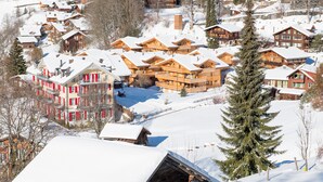 Un pueblo cubierto de nieve con chalets de madera, un edificio rojo con balcones y un gran abeto.