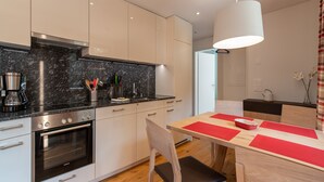 Una cocina moderna con horno empotrado, cafetera y comedor con mesa roja y blanca.