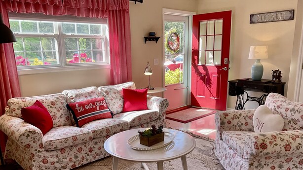 A cozy living room with floral-patterned sofas, a round coffee table, and a red door. - Lunas Flat  145 :Spotless, Sweet, Cozy & Comfy. Just renovated. (Aiken)