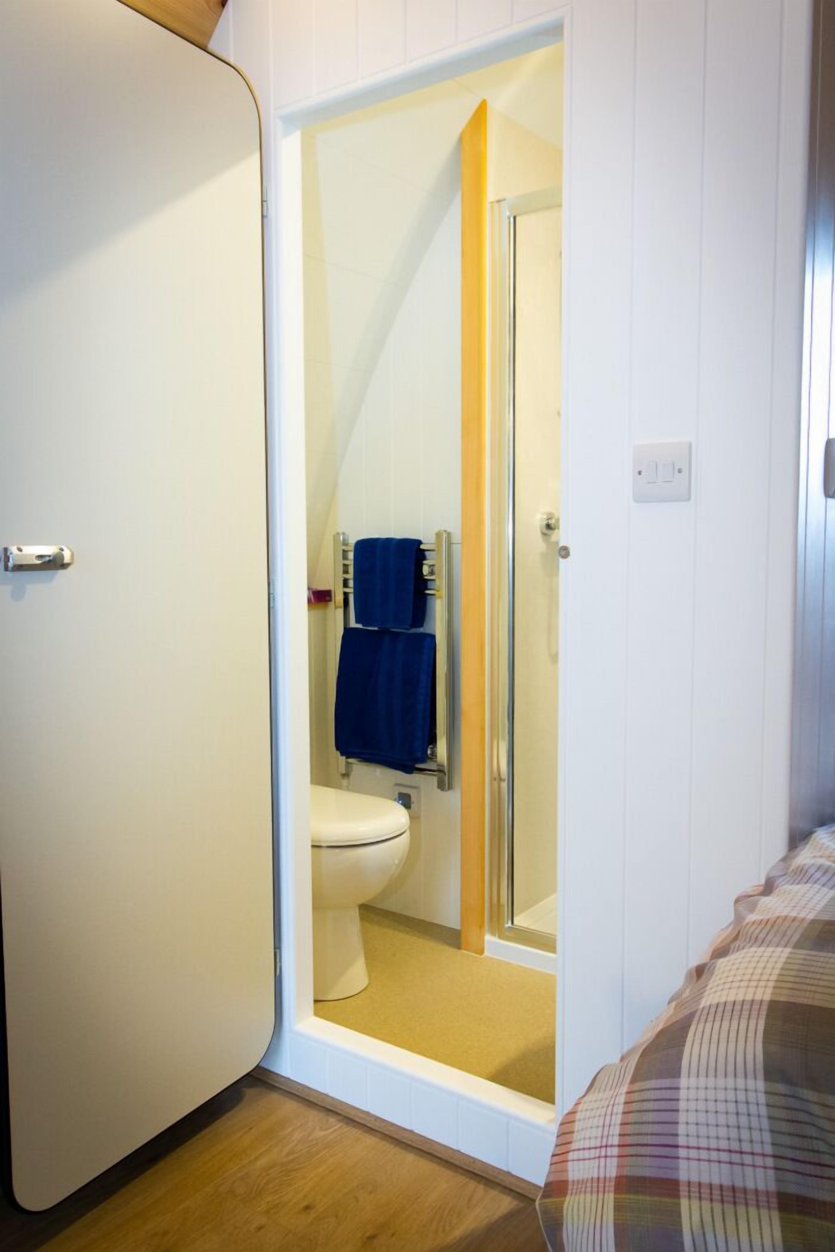 A small, compact bathroom with a toilet, a glass shower enclosure, and a towel rack.