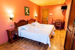 A double bed with white linens, two bedside tables, a wooden headboard, a small desk with a chair, a television mounted on the wall, and a wooden door. - Hotel Peña Pandos (Aller)