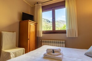 A hotel room with a bed, a wooden wardrobe, a television on top, and a window with curtains. - Hotel Peña Pandos (Aller)