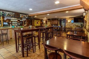 A restaurant with wooden tables and chairs, a bar area with shelves of bottles, and a stone wall with a TV. - Hotel Peña Pandos (Aller)