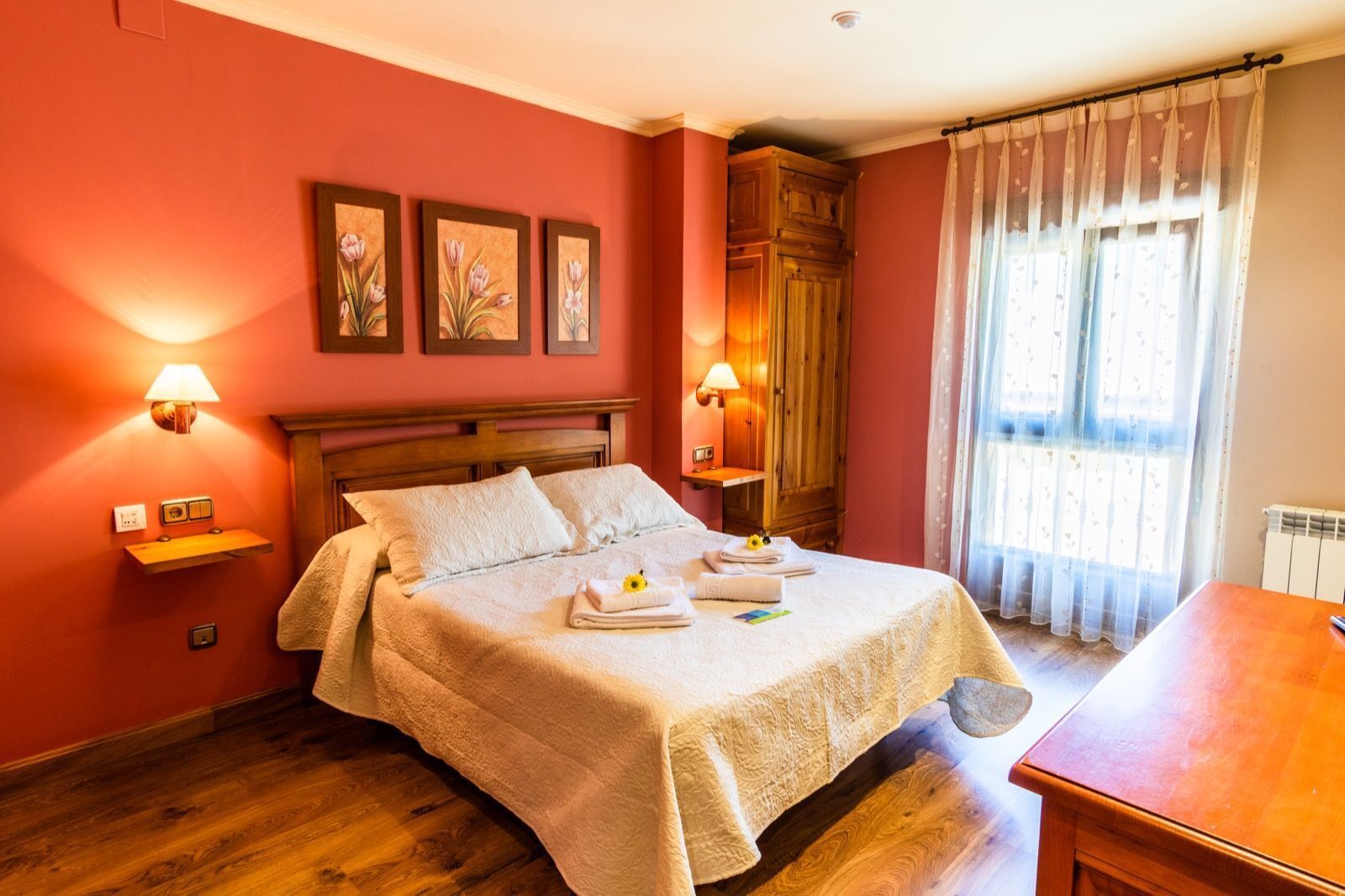 Una cama bien hecha con una colcha color beige, dos almohadas y una mesita con un arreglo floral.